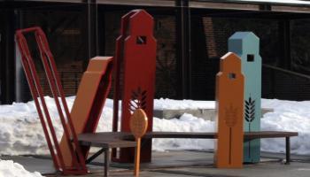 A bench sculpture with grain elevators for supports.