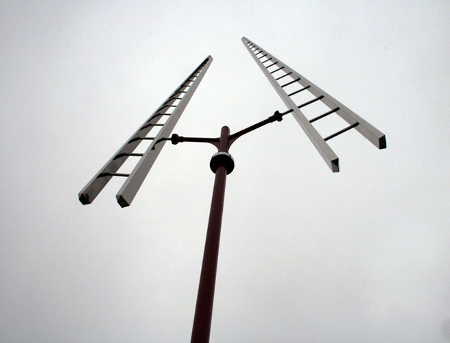 Sculpture of two ladders balanced at the top of a red pole.