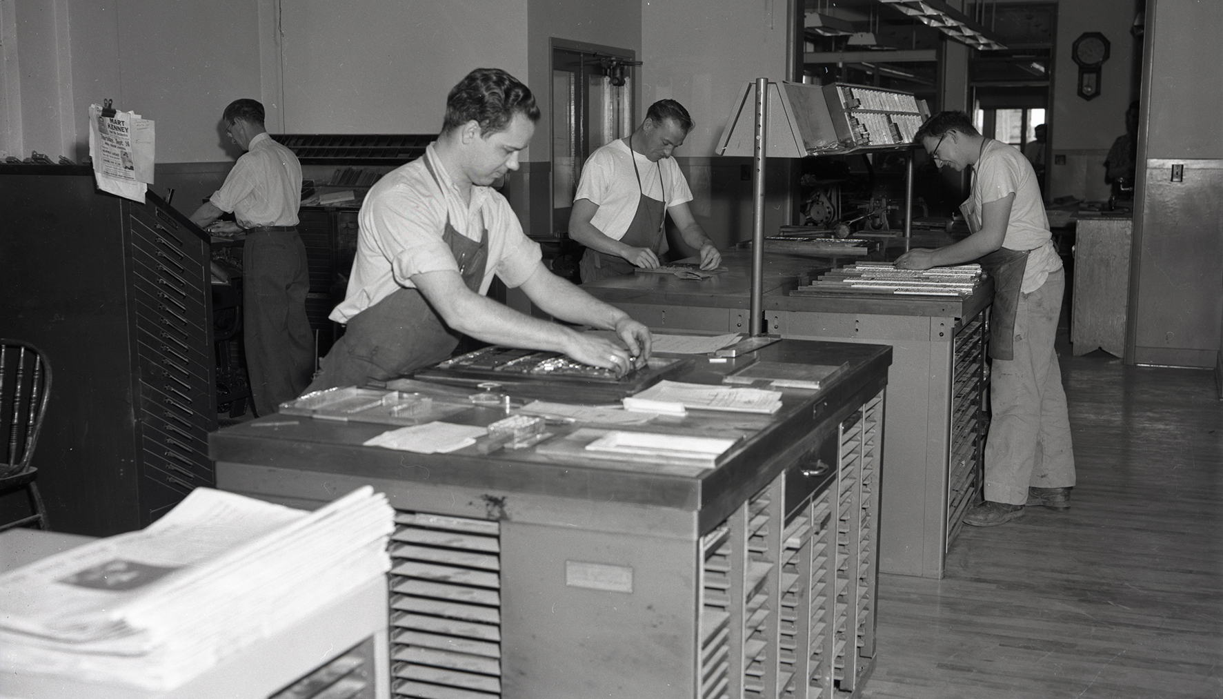 Black and white photo of men working at desks as typesetters for a newspaper, 1954