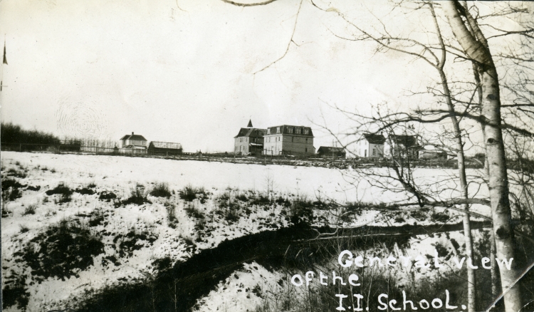 Black and white photo of the buildings at the Red Deer Indian Industrial School, before 1919, including a field in the foreground.
