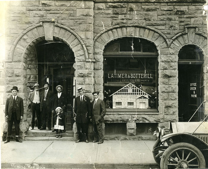 A group of men and a child standing outside a building downtown Red Deer in 1909. 