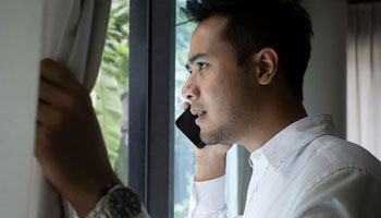 Man looking out his window reporting a crime on the phone