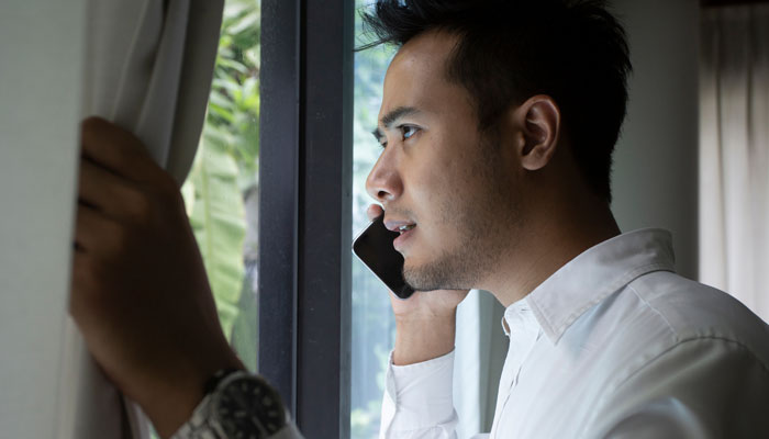 Photo of man peering out of his window while talking on the phone