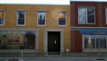 Street view of a building with a painted mural of store front shop windows with apartment windows above.