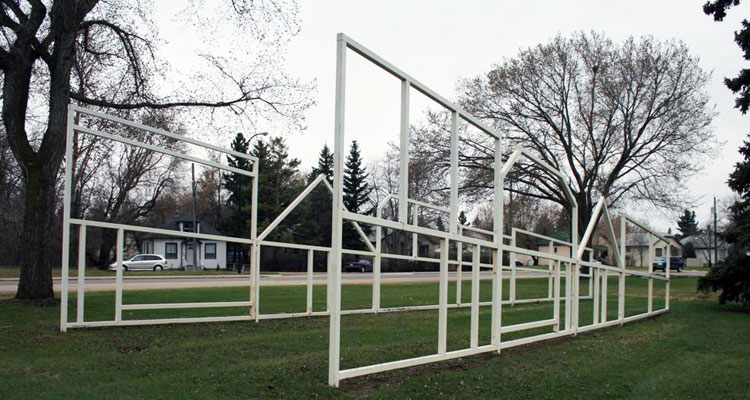 White sculpture of boards put together to form the outline of a city street with buildings and houses.