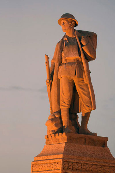 Photograph of the cenotaph of Major Frank Norbury taken at sunset. He is dressed in soldier apparel from the First World War.