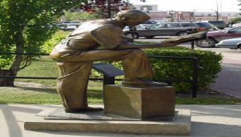 Side view of the sculpture of Francis Wright Galbraith, who is leaning his arm on his knee reading the newspaper and drinking a coffee.