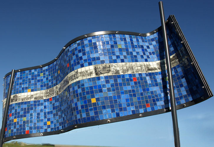 Blue side of a rectangle sculpture made up of glass tiles an the photo etched tiles of old photographs.